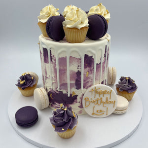 Purple and white birthday cake with purple macarons and bite size cupcakes